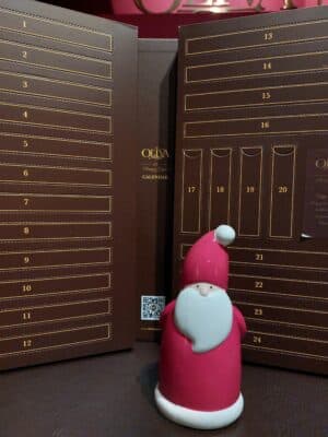 Porzellan-Weihnachtsmann steht vor dem offenen Zigarren-Adventskalender von 2025.